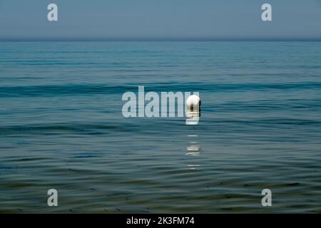 Minimalist image of a white buoy floating on the sea, seemingly isolated, with the horizon line dividing sky and sea in the background. Sicily summer. Stock Photo