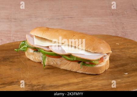 fresh submarine sandwiches with ham, cheese, bacon, tomatoes, lettuce, cucumbers and onions on dark wooden background Stock Photo