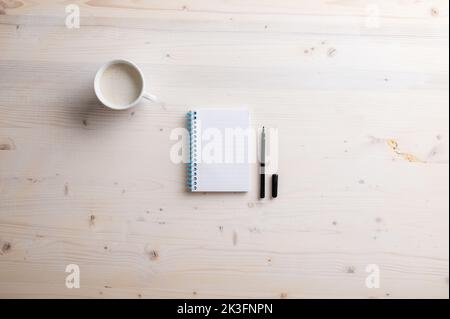 Blank spiral notebook and open black spiral pen placed on simple wooden desk with a cup of fresh coffee. Stock Photo
