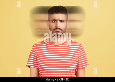 Triple exposure creative portrait of serious handsome bearded man in red t-shirt looking at camera with angry face. Mental health concept. Indoor studio shot isolated on yellow background. Stock Photo