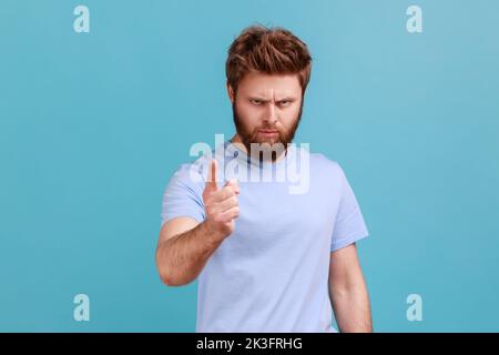 Portrait of strict serious young bearded man warning of mistake, looking at camera with admonishing finger and alarming, giving advice. Indoor studio shot isolated on blue background. Stock Photo