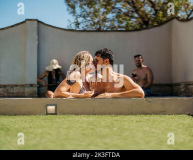 Caucasian couple kissing leaning on the edge of a swimming pool Stock Photo