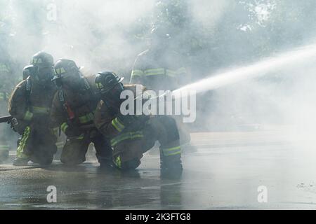 Firefighters with the 914th Fire Emergency Services work together to control a water hose while putting out an aircraft structure fire at a training facility in Rochester, New York, August 24, 2022.  Training for an aircraft fire enhances readiness of our firefighters by giving them hands on experience on how to suppress and ultimately put out the flames as quickly as possible to prevent further damage or injuries. (U.S. Air Force Photo by Airman Kylar Vermeulen) Stock Photo