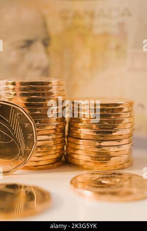 Stacks of Canadian one dollar coins and faded five dollar currency bank note in background. Stock Photo