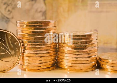 Stacks of Canadian one dollar coins and faded five dollar currency bank note in background. Stock Photo