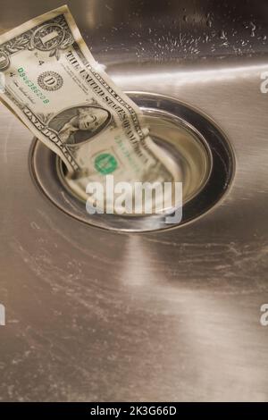 US Dollar going down the drain in stainless steel kitchen sink. Stock Photo