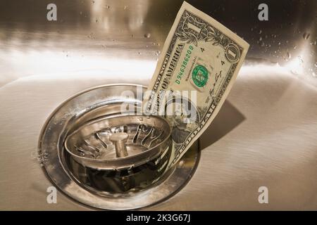 US Dollar going down the drain in stainless steel kitchen sink. Stock Photo