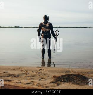 Rearview of spear fisherman standing in the water with a speargun. Adventurous young man getting ready to go spearfishing in the sea. Stock Photo