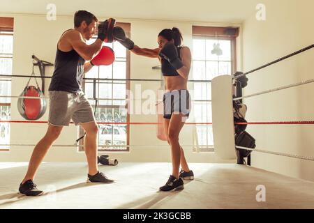 Male trainer helping a young female boxer with reverse punches in a boxing ring. Boxing coach training a sporty young woman in a gym. Stock Photo