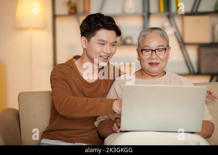 Smiling teenage boy with brackets helping grandmother learning how to work on laptop Stock Photo