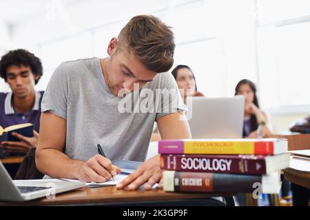 Sure of study success. A handsome young student sitting at a desk with her textbooks. Stock Photo