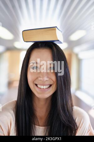 Shes excited to learn. Portrait of an attractive young student balancing a book on her head. Stock Photo