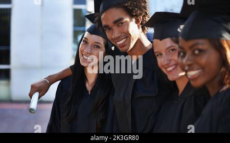 Weve officially graduated. A group of smiling college graduates standing together in cap and gown. Stock Photo