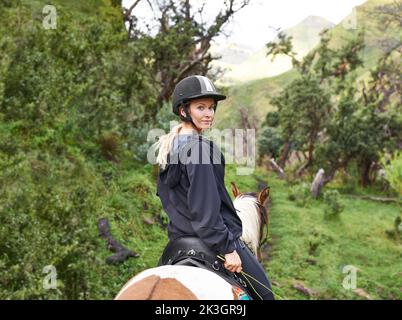 Horse riding in the outback. An attractive young woman going for a horse ride on a mountain trail. Stock Photo