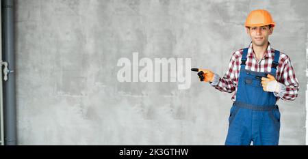Young arabic man over grey wall wearing contractor uniform and safety helmet happy with smile showing with thumb up to the side with happy face smilin Stock Photo