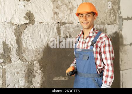 Portrait of smiling builder worker plasterer holding trowel to plastering cement wall in construction site. building construction work and industry co Stock Photo