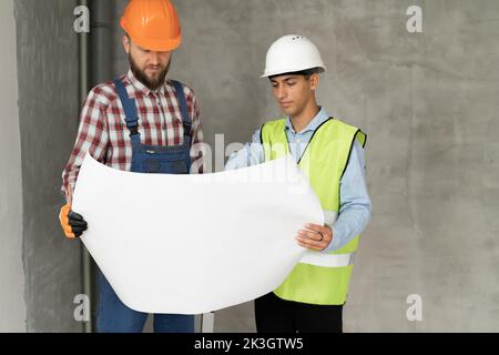 Architect and construction engineer or surveyor discussion plans and blueprints. Two men are wearing hardhats and are standing on the construction sit Stock Photo