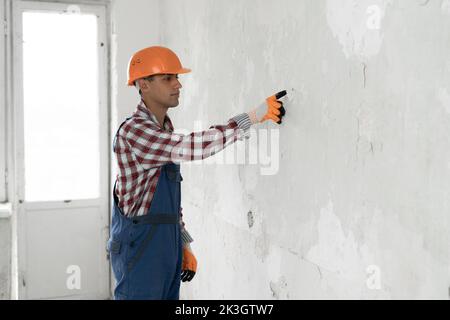 Young arabic man over grey wall wearing contractor uniform and safety helmet pointing and showing with finger to the wall empty space, copy space Stock Photo