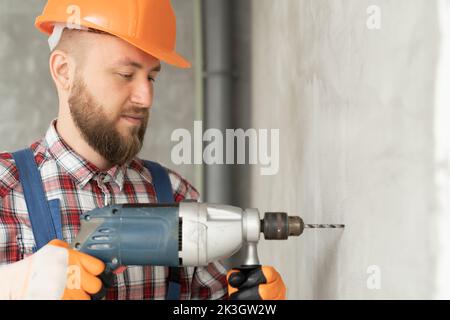 portrait of a young foreman working with a drill in the room, a builder drilling a wall makes repairs in the house, repair service and construction co Stock Photo