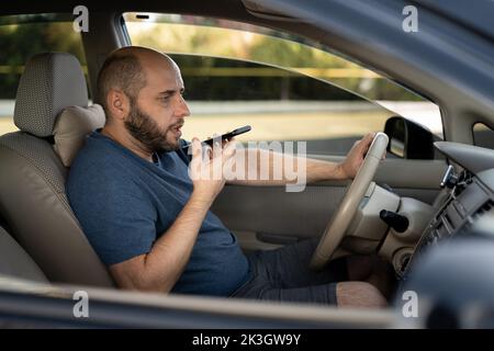 man driving his new car recording the voice message at smartphone, driver using voice command recorder on phone Stock Photo