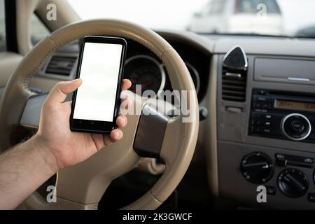 man using mobile smart phone, checking address location via navigator application, driving a car. Driver hand holding smartphone white screen mockup Stock Photo