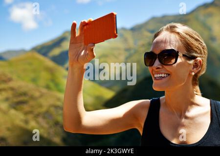 Capturing mountainside memories. A young woman taking a picture in the mountainside. Stock Photo