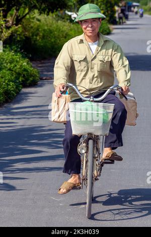 Cyclist wearing bamboo hat on country road, rural Hai Phong, Vietnam Stock Photo