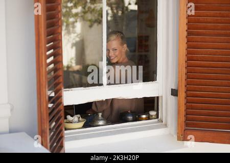 In a peaceful frame of mind. A young woman looking through her window. Stock Photo