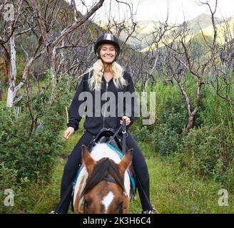 Horse riding in the outback. An attractive young woman riding a horse along a mountain trail. Stock Photo