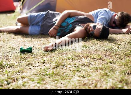 I didnt fall the floor just needed a hug. two young men lying on the grass after drinking too much at an outdoor festival. Stock Photo
