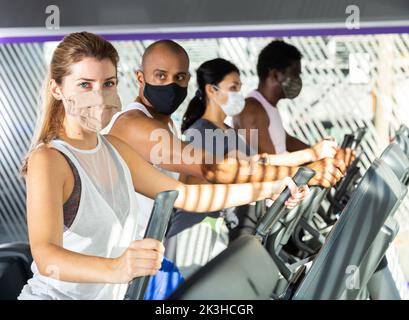 Active people in protective masks having running elliptical trainer class in club Stock Photo