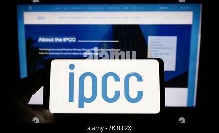 Person holding mobile phone with logo of Intergovernmental Panel on Climate Change (IPCC) on screen in front of web page. Focus on phone display. Stock Photo