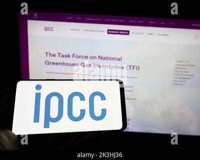 Person holding cellphone with logo of Intergovernmental Panel on Climate Change (IPCC) on screen in front of webpage. Focus on phone display. Stock Photo