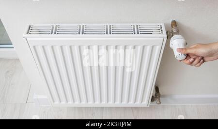 A woman regulates the gas heating in the room in order to save gas energy, taking into account the sanctions. Comfortable heating in the house. Stock Photo