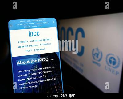 Person holding mobile phone with webpage of Intergovernmental Panel on Climate Change (IPCC) on screen with logo. Focus on center of phone display. Stock Photo