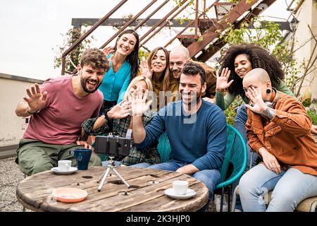 Multiethnic group of friends saluting on a conference video call sitting outdoors in the terrace - people and technology concept Stock Photo