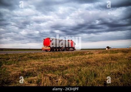 New red truck with a tanker truck transports gasoline against the background of the cloudy sky in the evening. Dangerous goods transport industry. Cop Stock Photo