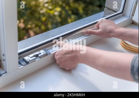 a woman glues a sealing rubber tape on a window in a living room. Stock Photo