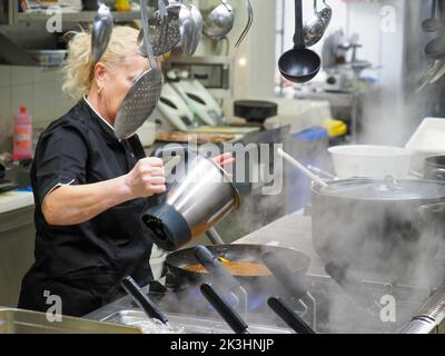 chef in white uniform pouring boiled spaghetti into pan wok for cooking pasta with vegetables Stock Photo