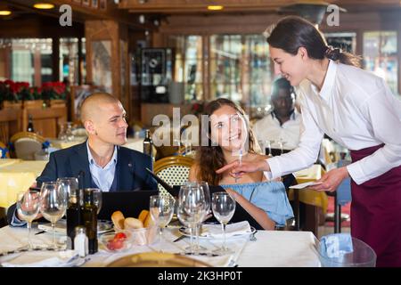 Young positive waitress taking table order from guests Stock Photo
