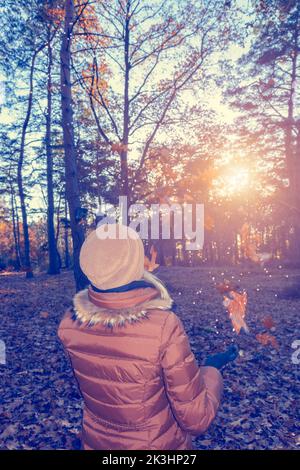 Young woman in warm clothes having fun with autumn leaves in the forest. Stock Photo