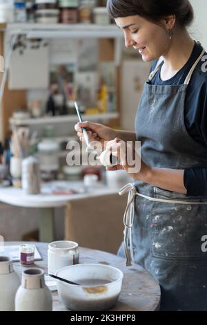 Young ceramist woman enjoys making and painting handmade products from clay in workshop.  Stock Photo