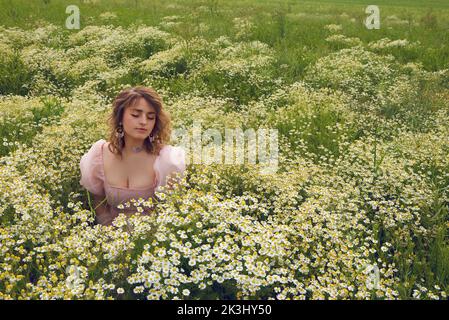 Young blonde woman wearing a pink puffy dress in a flower field in summer Stock Photo