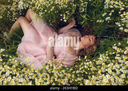Young blonde woman wearing a pink puffy dress in a flower field in summer Stock Photo