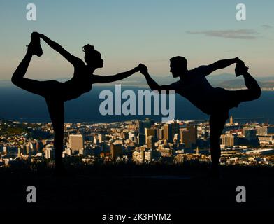 Silhouette of couple stretching and doing yoga at sunrise in the city. Man and woman training, exercising and doing workout together at sunset. People Stock Photo
