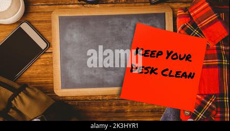 Composite of keep your desk clean on sticky note with slate, cellphone with t-shirt on table Stock Photo