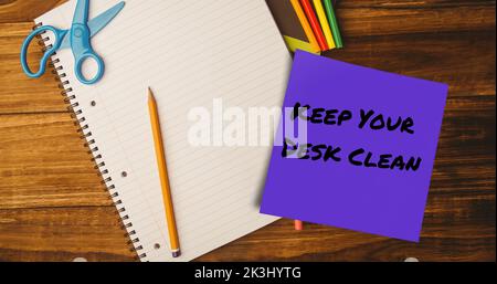 Composite of keep your desk clean on sticky note with pencil, scissors and notebook on table Stock Photo