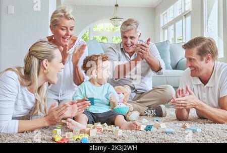 Family, clapping hands and baby playing with toys while sitting on the living room floor. Love, care and happy people cheering for child development Stock Photo