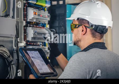 Man, an electrical technician working in a switchboard with fuses. Stock Photo