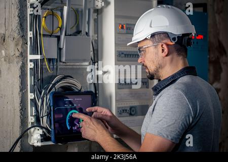 Man, an electrical technician working in a switchboard with fuses, uses a tablet. Stock Photo